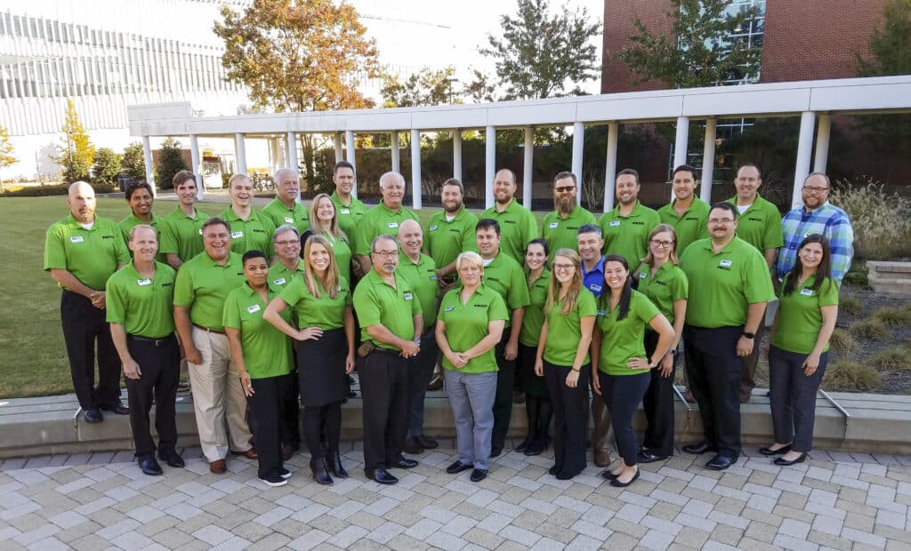 A group picture of 30 people, all wearing matching lime green polo shirts, in an outdoor courtyard.