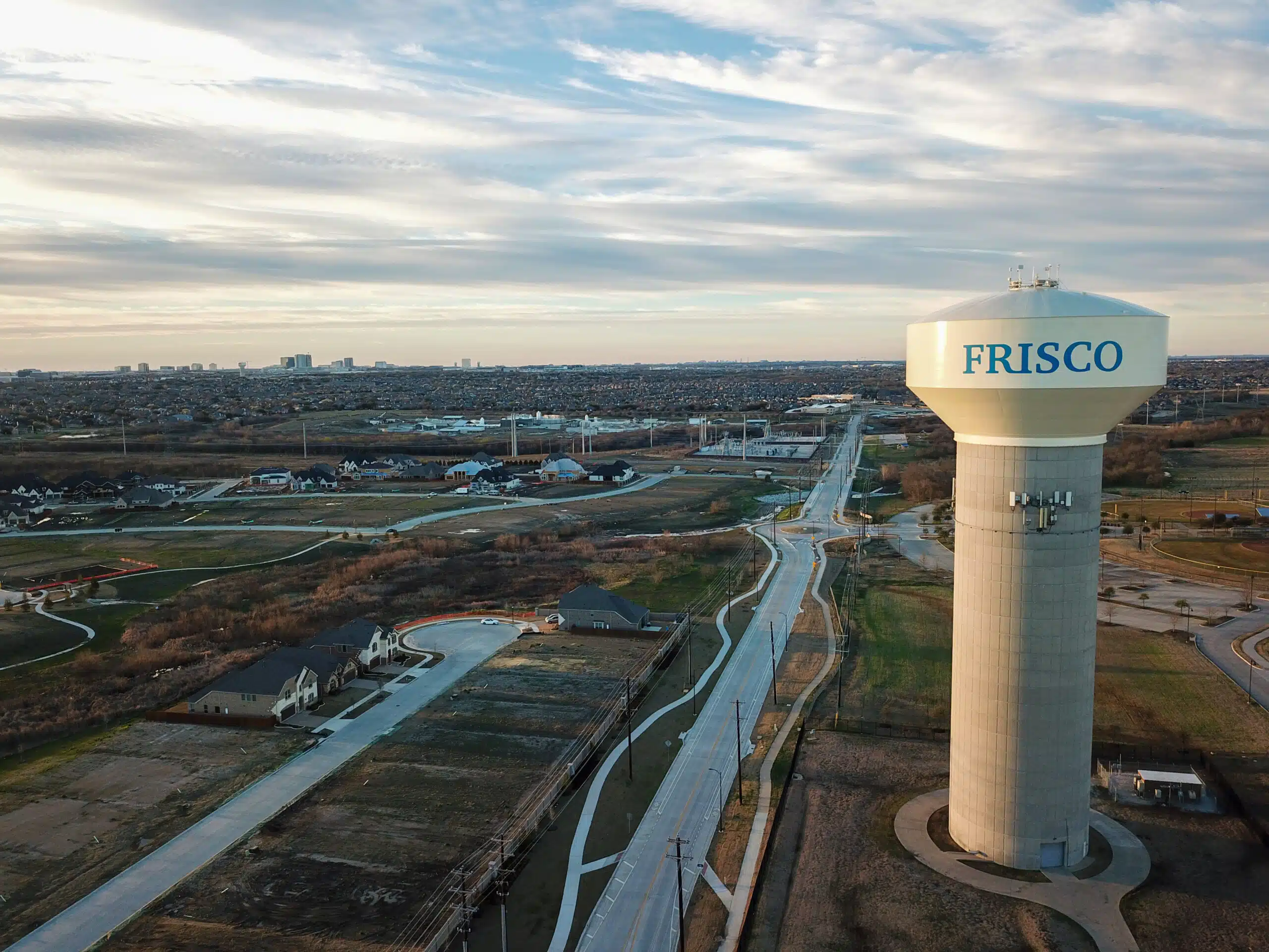 An aerial view of new subdivisions being developed in Frisco, Texas. A Frisco water tower is in the foreground and office towers are on the horizon.